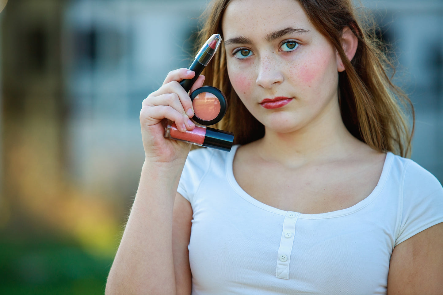 Woman holding makeup products outdoors with a blurred background